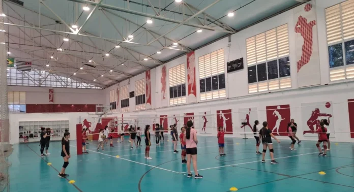 Meninas praticando vôlei em quadra poliesportiva durante aula do Projeto Raízes em Osasco